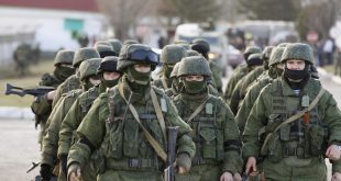 Military personnel, believed to be Russian servicemen, walk outside the territory of a Ukrainian military unit in the village of Perevalnoye outside Simferopol